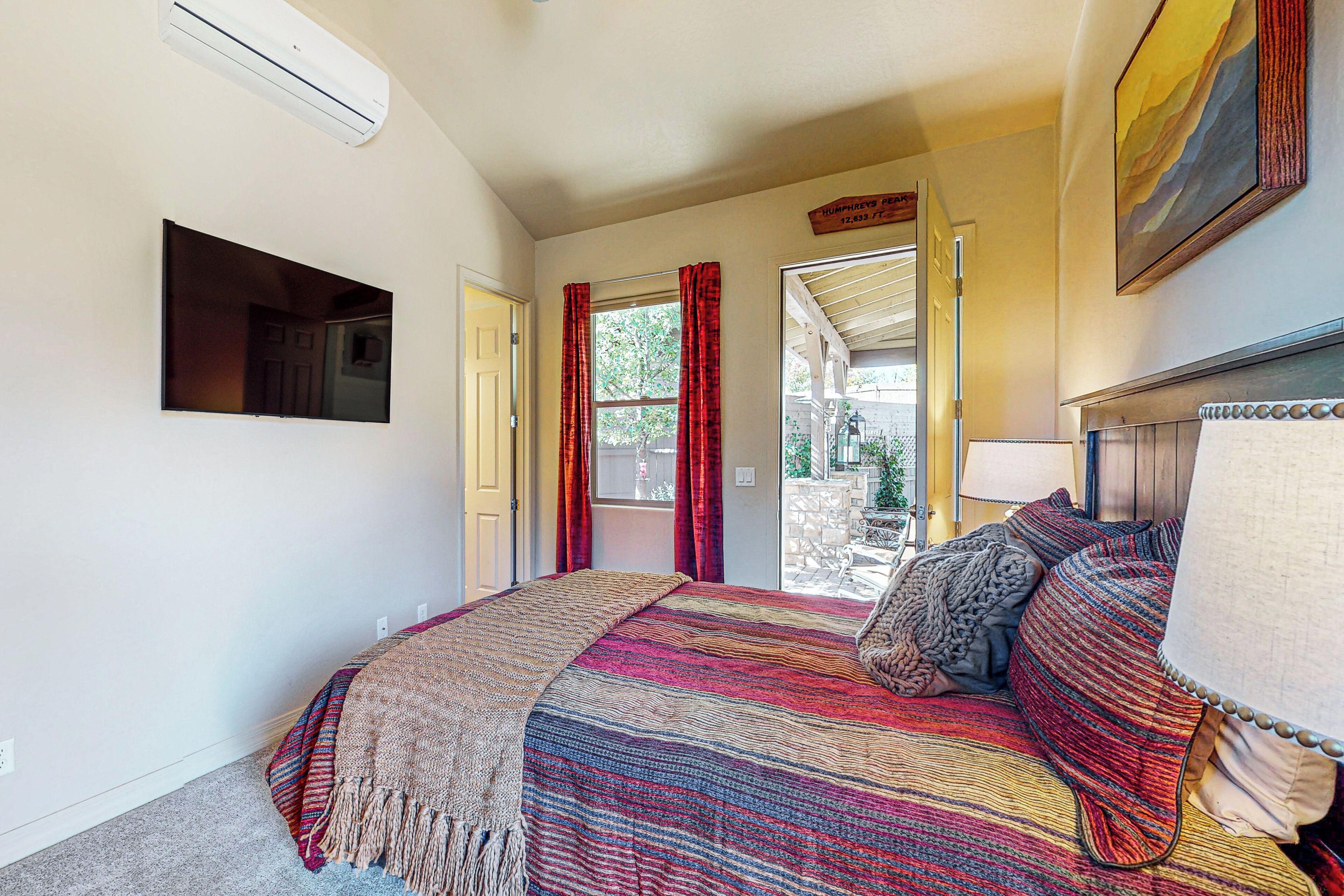 A bedroom with a large bed, a TV mounted on the wall, and a door leading to an outdoor area.