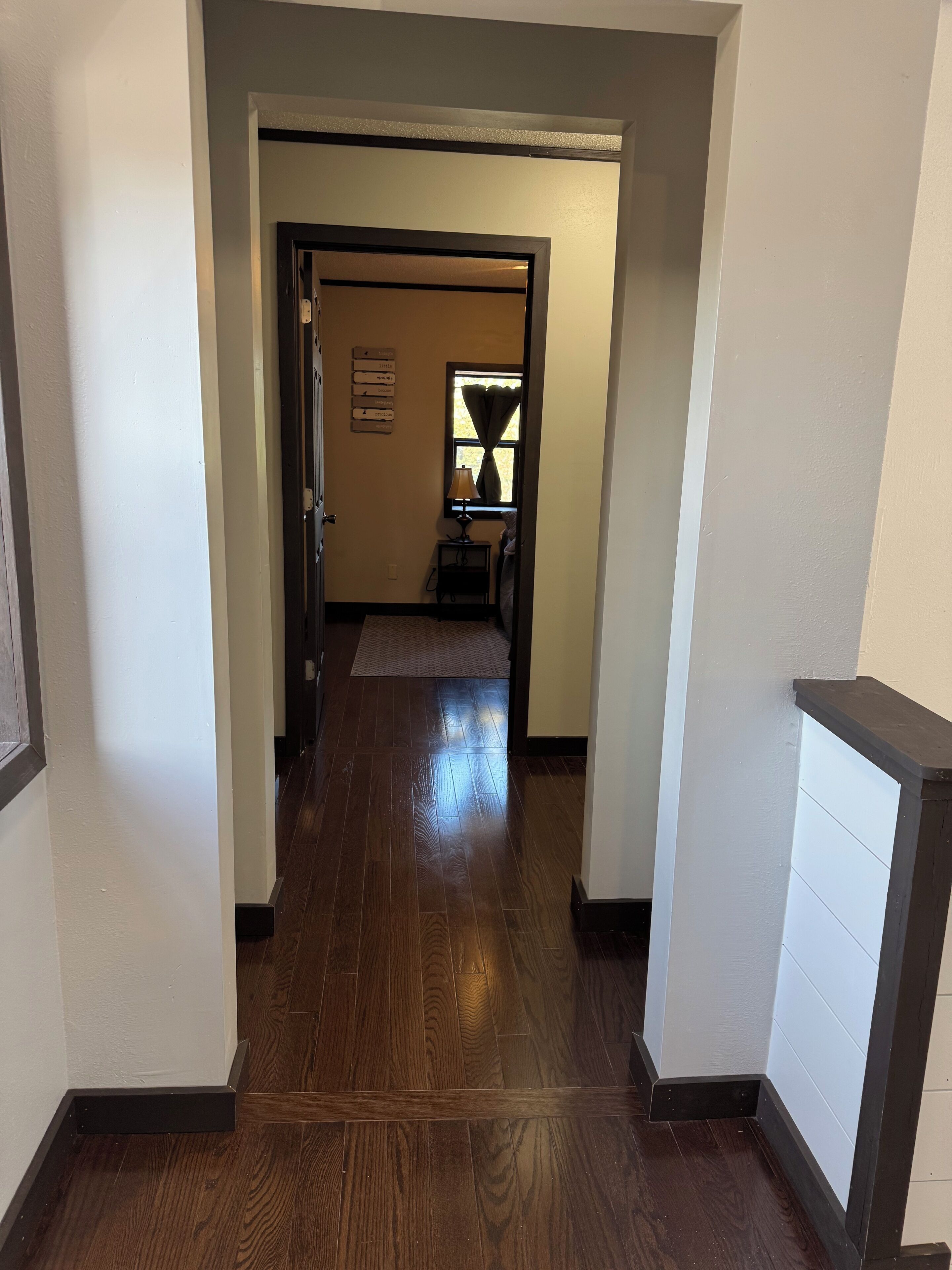 A hallway with wooden flooring, a door at the end, and a small table with a lamp.