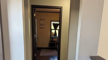 A hallway with wooden flooring, a door at the end, and a small table with a lamp.