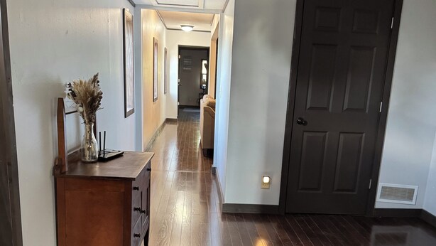 A hallway with wooden flooring, a dark door, and a small table with a vase. - Charming 3-bedroom upstairs apartment in welcoming Fennimore. (Fennimore)