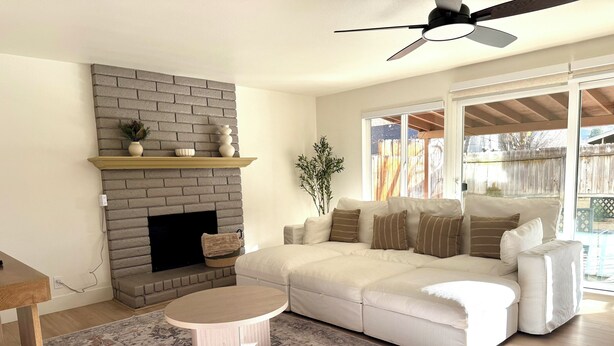 A living room with a brick fireplace, a white sofa, a round coffee table, and a ceiling fan. - NEW 4BR Cozy Home close to everything! Pet-friendly & remote work friendly (Reno)