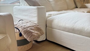 A modern living room with a sectional sofa, a small side table, and a view of the outdoors through a large window. - NEW 4BR Cozy Home close to everything! Pet-friendly & remote work friendly (Reno)