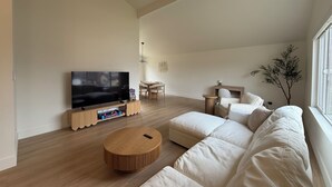 A modern living room with a large flat-screen TV, a round wooden coffee table, and a beige sectional sofa. - NEW 4BR Cozy Home close to everything! Pet-friendly & remote work friendly (Reno)