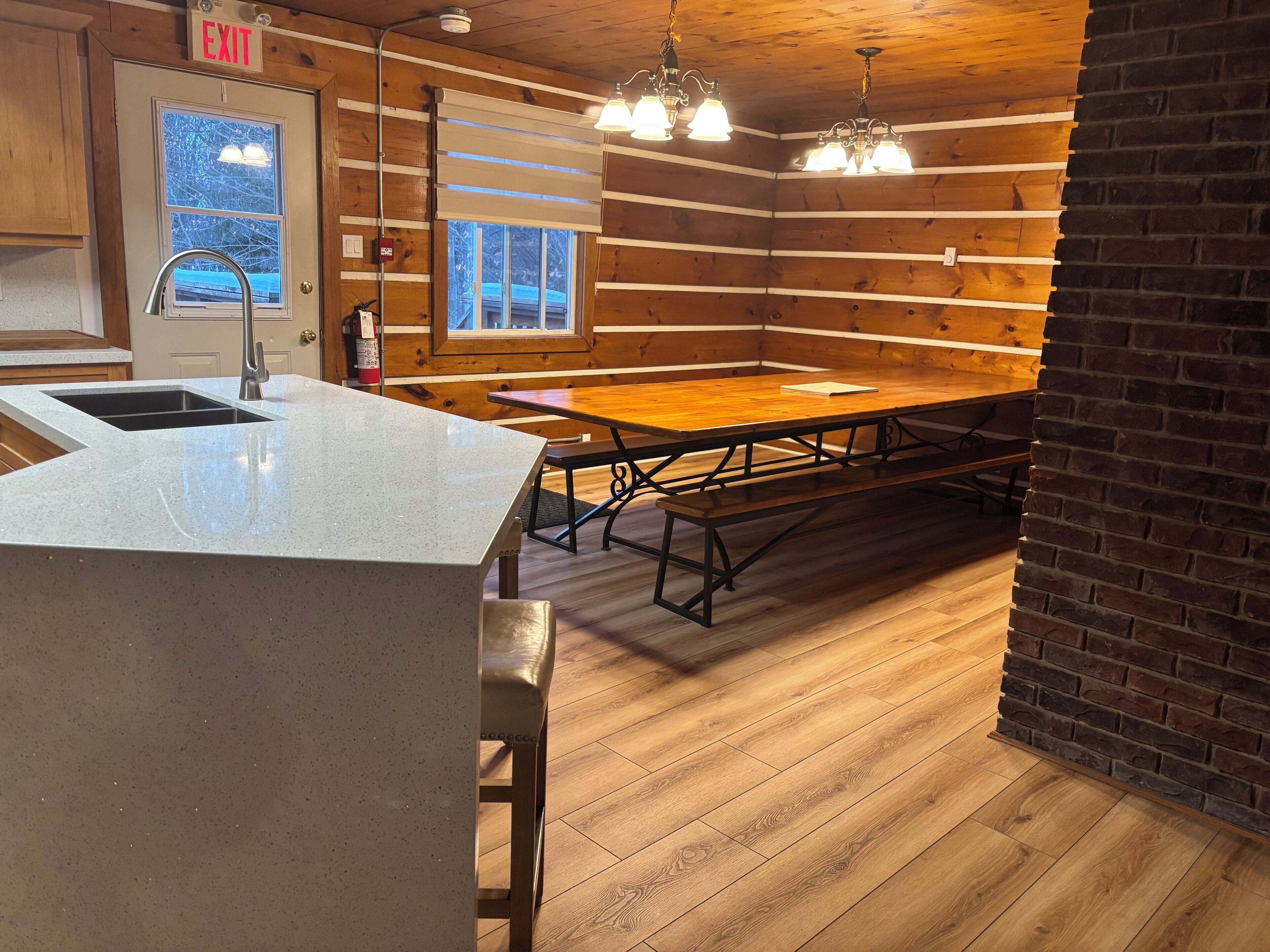 A cabin-style kitchen with a sink, wooden table, benches, and a window with a view.