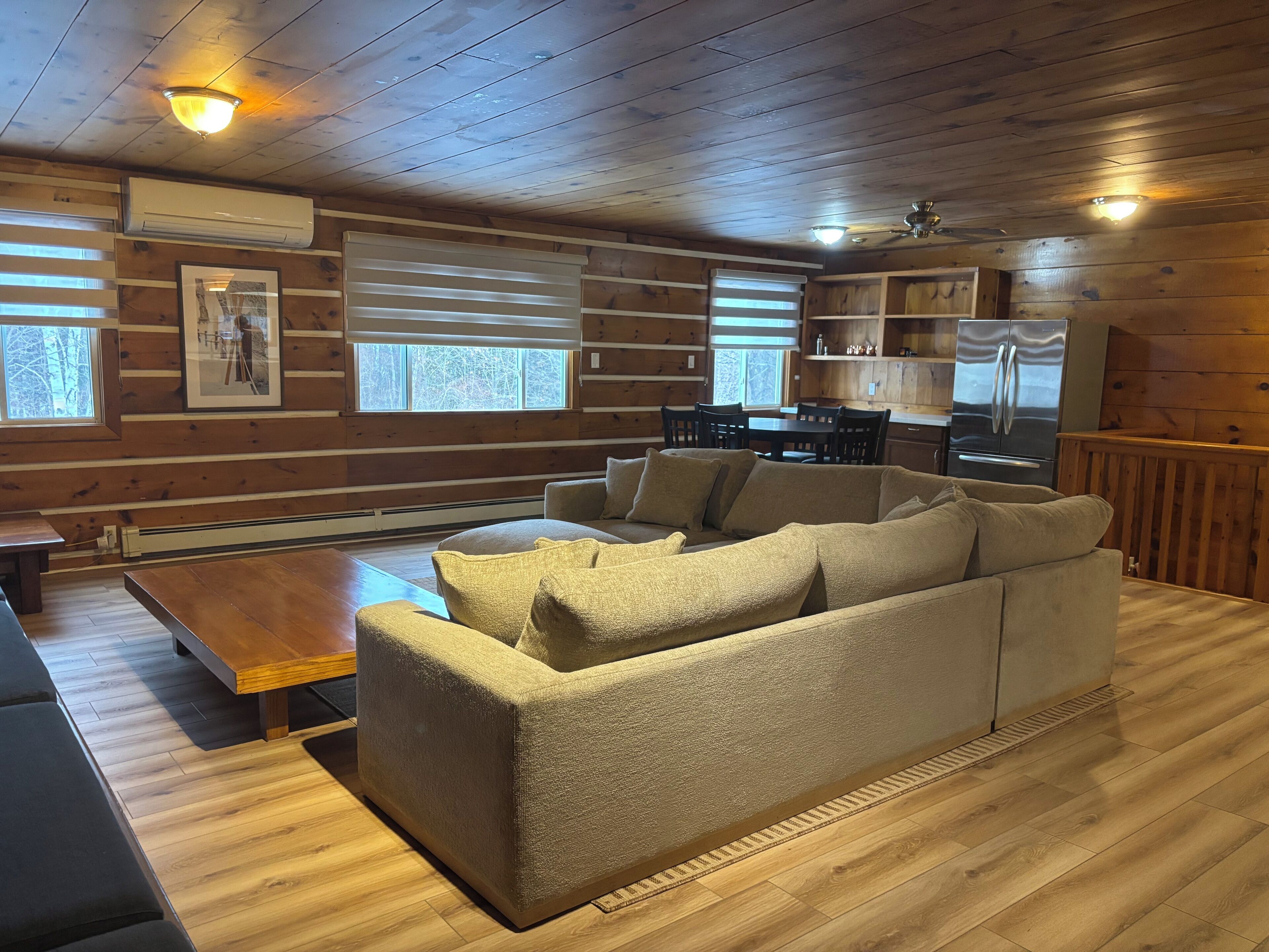 A cozy cabin interior with a sofa, wooden floors, a dining table, and a kitchen area.