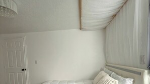 Une chambre à coucher comprenant un lit, une table de chevet, une commode, une porte et un luminaire au plafond.