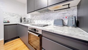 A modern kitchen with dark cabinetry, a marble backsplash, and stainless steel appliances. - Host Stay Apartment 1 Stanley Street (Liverpool)