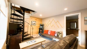 A living room with a sofa, a coffee table, a fireplace, a staircase, and a wall with geometric decorations.
