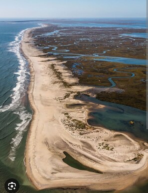 An aerial view of a coastal area with a sandy beach, a winding water body, and sparse vegetation. - Come RELAX at our brand new bay front 3-bedroom home in charming Cedar Island. (Cedar Island)