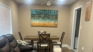 A living room with a leather sofa, a wooden dining table with chairs, a ceiling fan, and a colorful abstract painting on the wall. - 3 Bedroom Home with Long Driveway  & Covered Deck (Jackson)