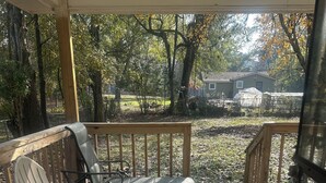 A wooden deck with two white plastic chairs and a table, overlooking a yard with trees and a house in the background. - 3 Bedroom Home with Long Driveway  & Covered Deck (Jackson)