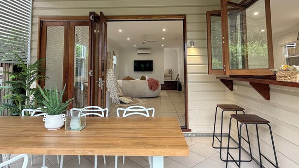 Un coin repas avec une table et des chaises en bois, une plante en pot, et une vue sur une autre pièce où se trouvent un lit et un téléviseur.