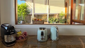 Un comptoir de cuisine avec une machine à café, deux grille-pain et un panier de fruits.