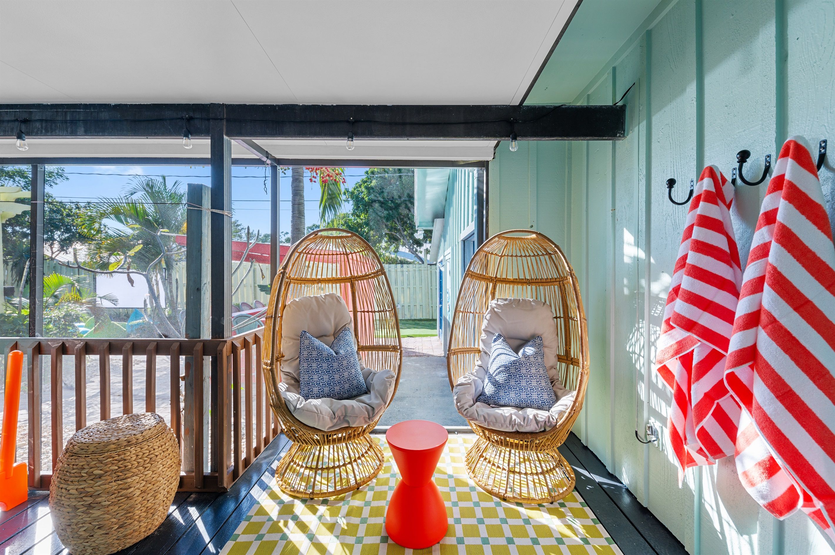 A balcony with wicker chairs, a red table, and striped towels on hooks.