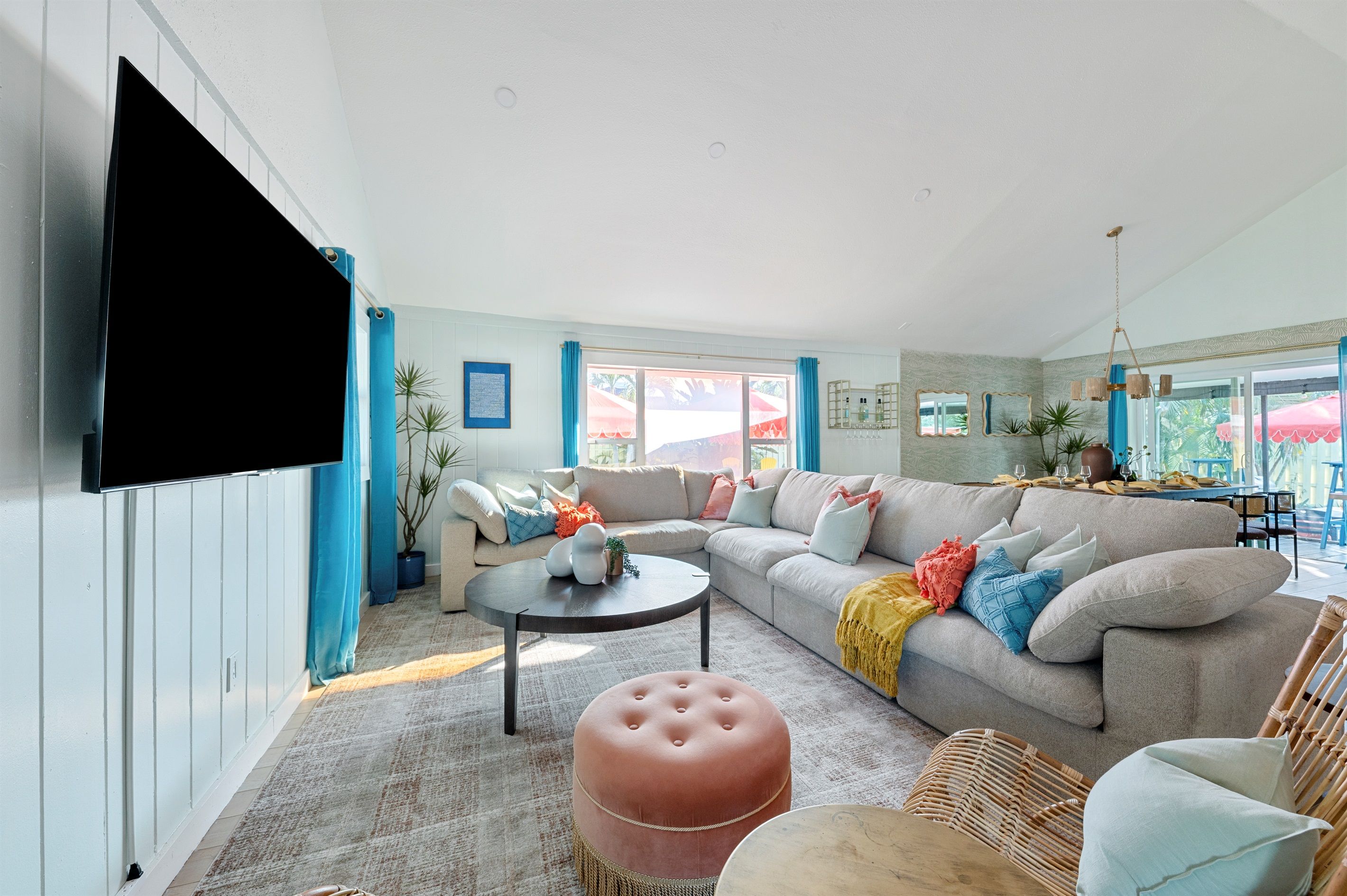 A living room with a large flat-screen TV, a sectional sofa, a round coffee table, and a wicker chair.