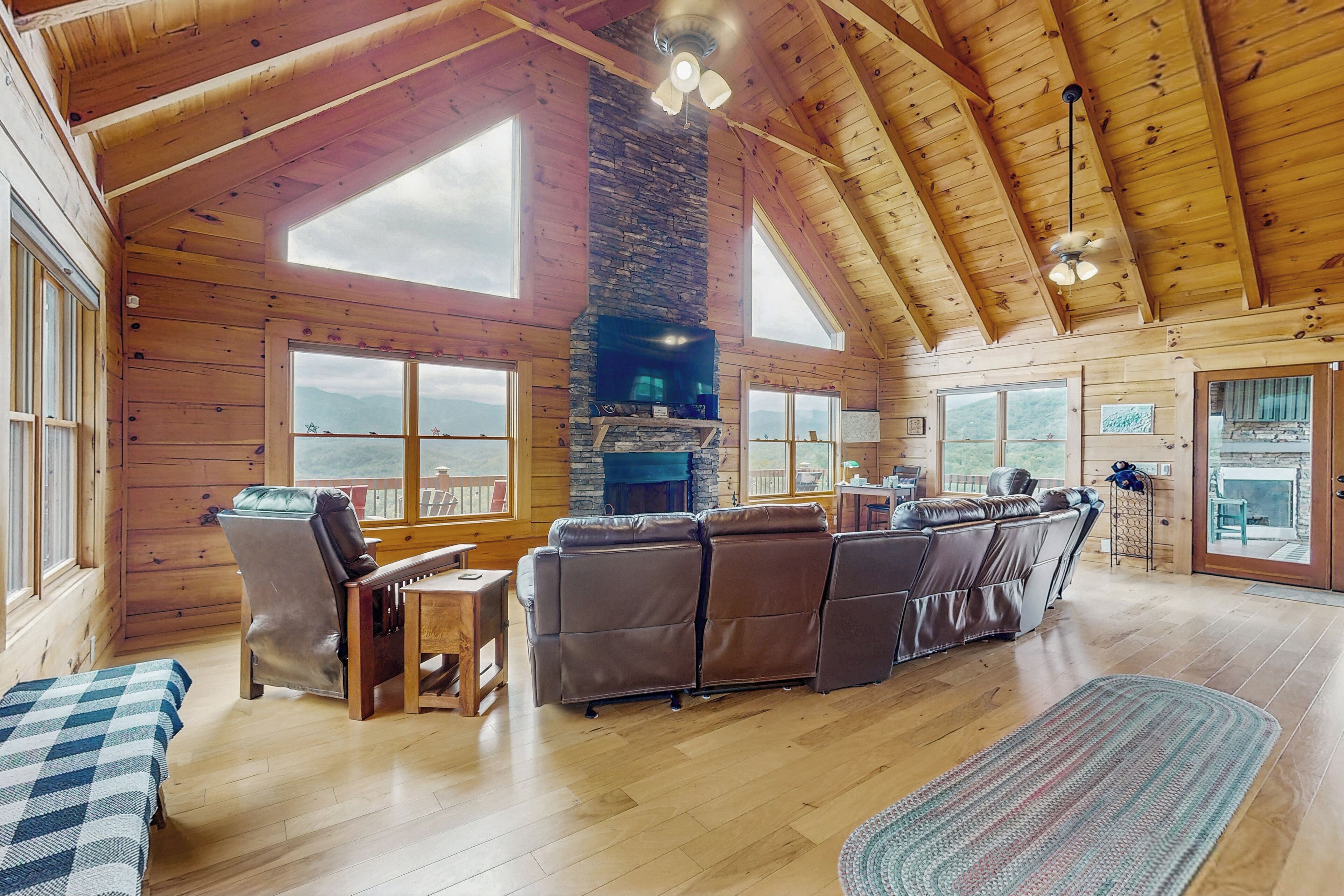 A spacious wooden cabin with a fireplace, leather seating, and large windows offering mountain views.