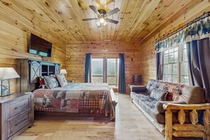 A log cabin bedroom with a bed, a sofa, a ceiling fan, and a window with curtains. - Theater + Arcade! 'Tri-Star Lodge' in Gatlinburg (Gatlinburg)