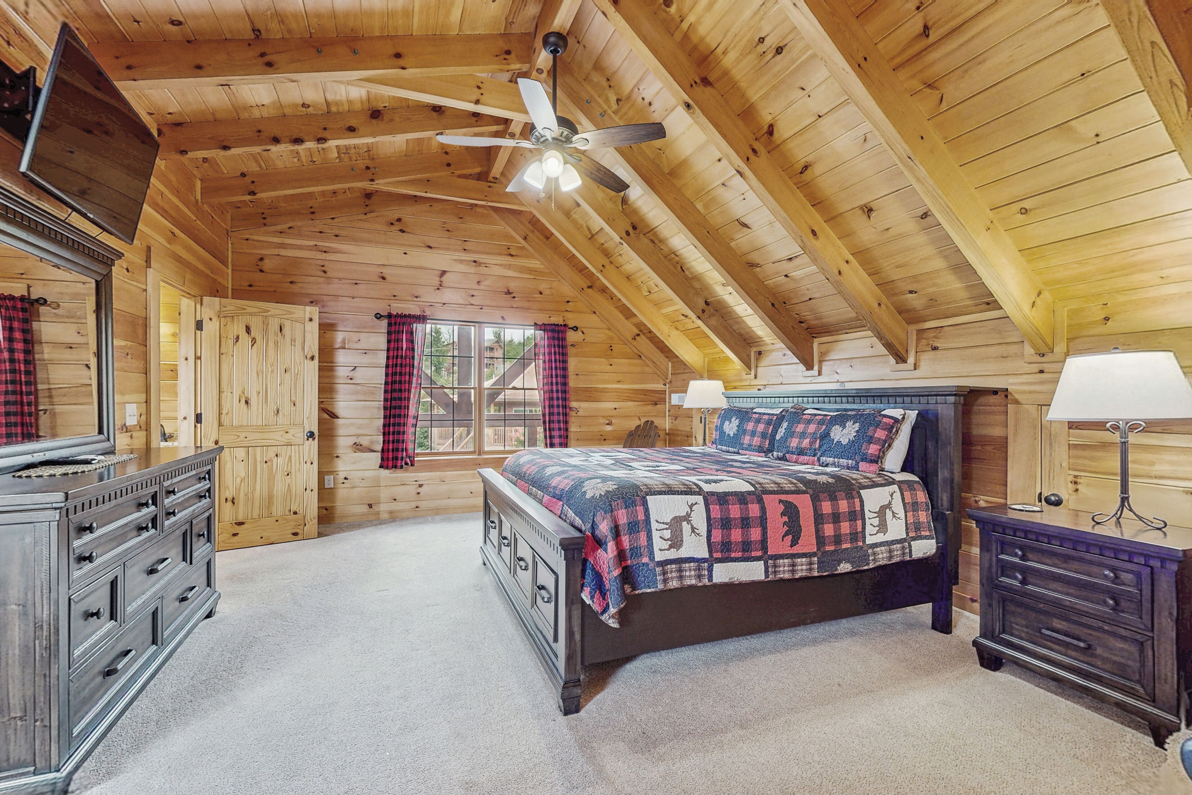 A cozy bedroom with a wooden ceiling, a bed with a quilt, a dresser, and a nightstand with a lamp.