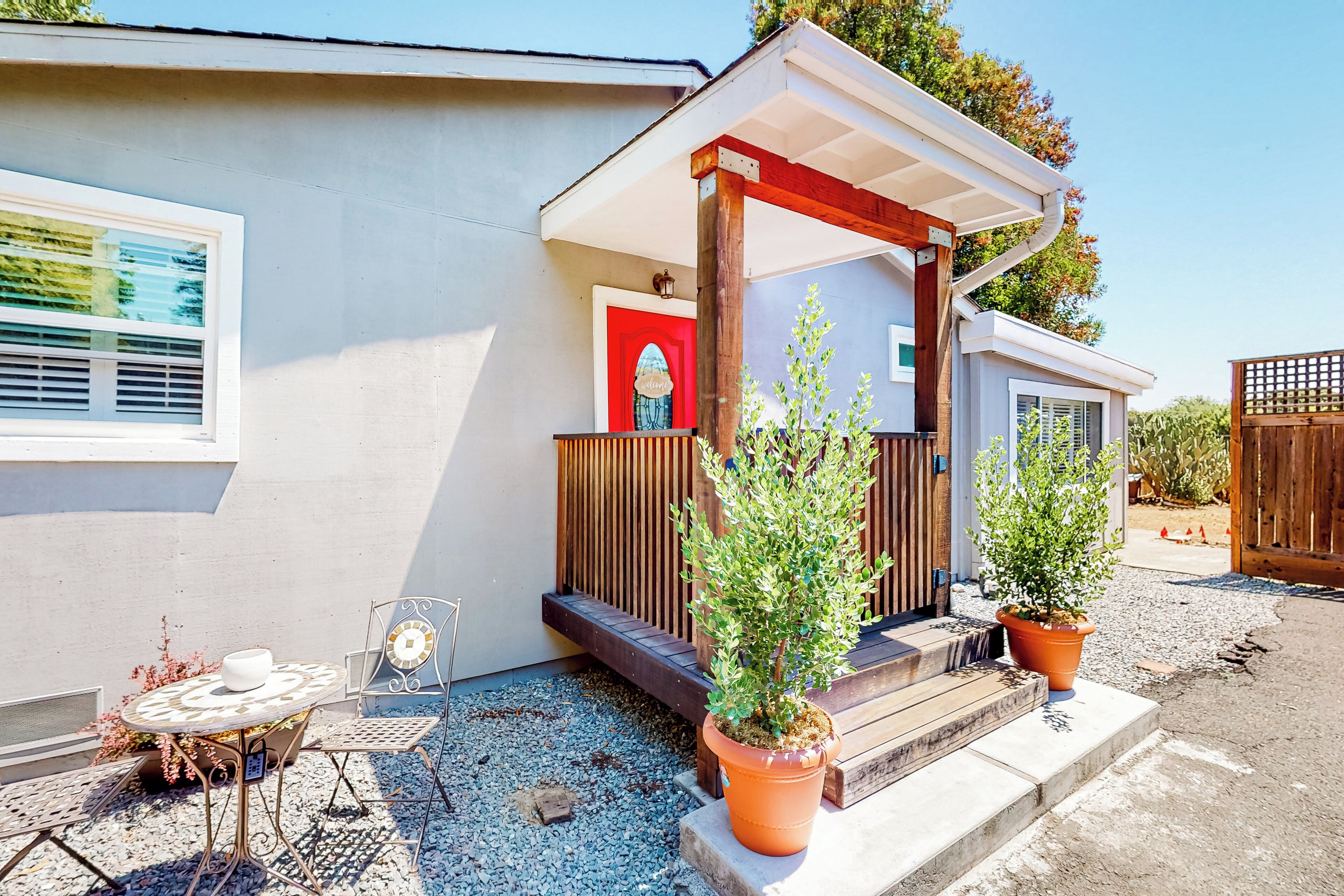 A small house with a porch, a table with chairs, and two potted plants.