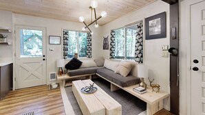 Un accogliente soggiorno con un divano componibile, una panca in legno, un tavolino da caffè e una grande finestra vista alberi.