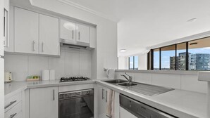 A modern kitchen with white cabinetry, a built-in oven, a dishwasher, and a stainless steel sink. - APARTMENT IN PARRAMATTA (Parramatta)