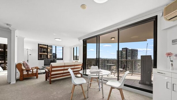 A modern apartment with a balcony, a sofa, a dining table, and a TV. - APARTMENT IN PARRAMATTA (Parramatta)