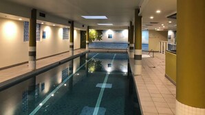 An indoor swimming pool with clear water, surrounded by walls with windows and a mural of a beach scene. - APARTMENT IN PARRAMATTA (Parramatta)