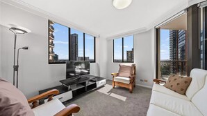 A modern living room with a flat-screen TV, a sofa, a chair, and a floor lamp. - APARTMENT IN PARRAMATTA (Parramatta)