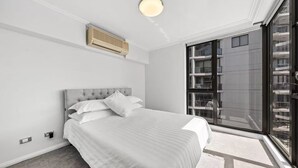 A modern bedroom with a large bed, a ceiling air conditioner, and a view of a building through a glass door. - APARTMENT IN PARRAMATTA (Parramatta)
