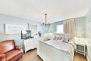 Ein Schlafzimmer mit Bett, Fernseher, Schminktisch, Stuhl und einer Chandelier.