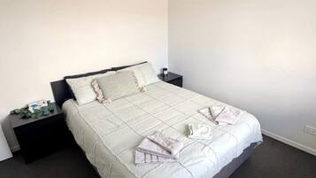 A bedroom with a bed, dark nightstands, a ceiling fan, and a plain wall.