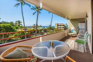 Ein Balkon mit Glastisch, Korbstühlen und Blick auf das Meer und Palmen.