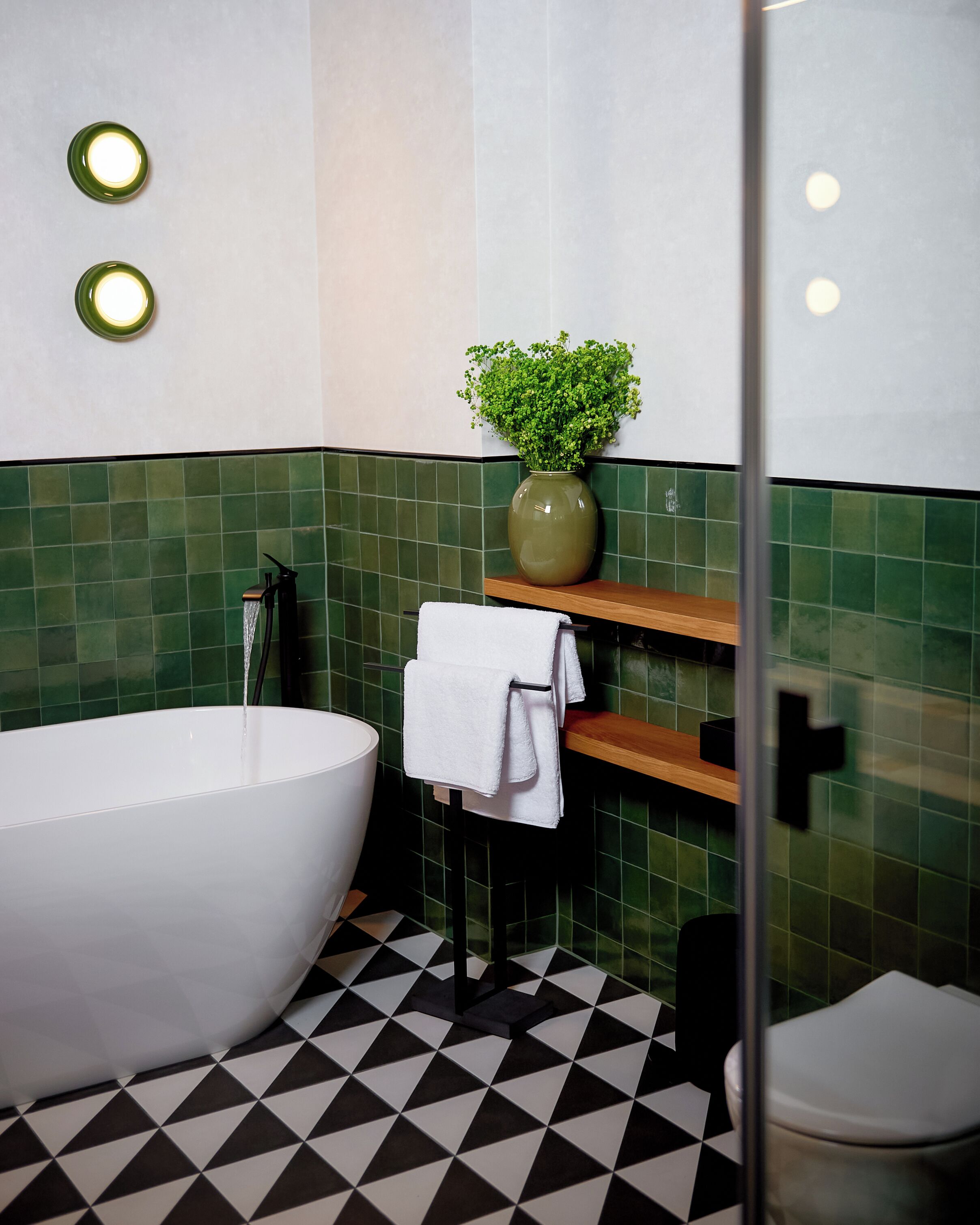A bathroom with a freestanding bathtub, a glass shower enclosure, a green tiled wall, and a black and white checkered floor.