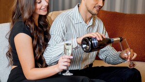 A couple sitting on a sofa with a bottle of champagne and glasses.