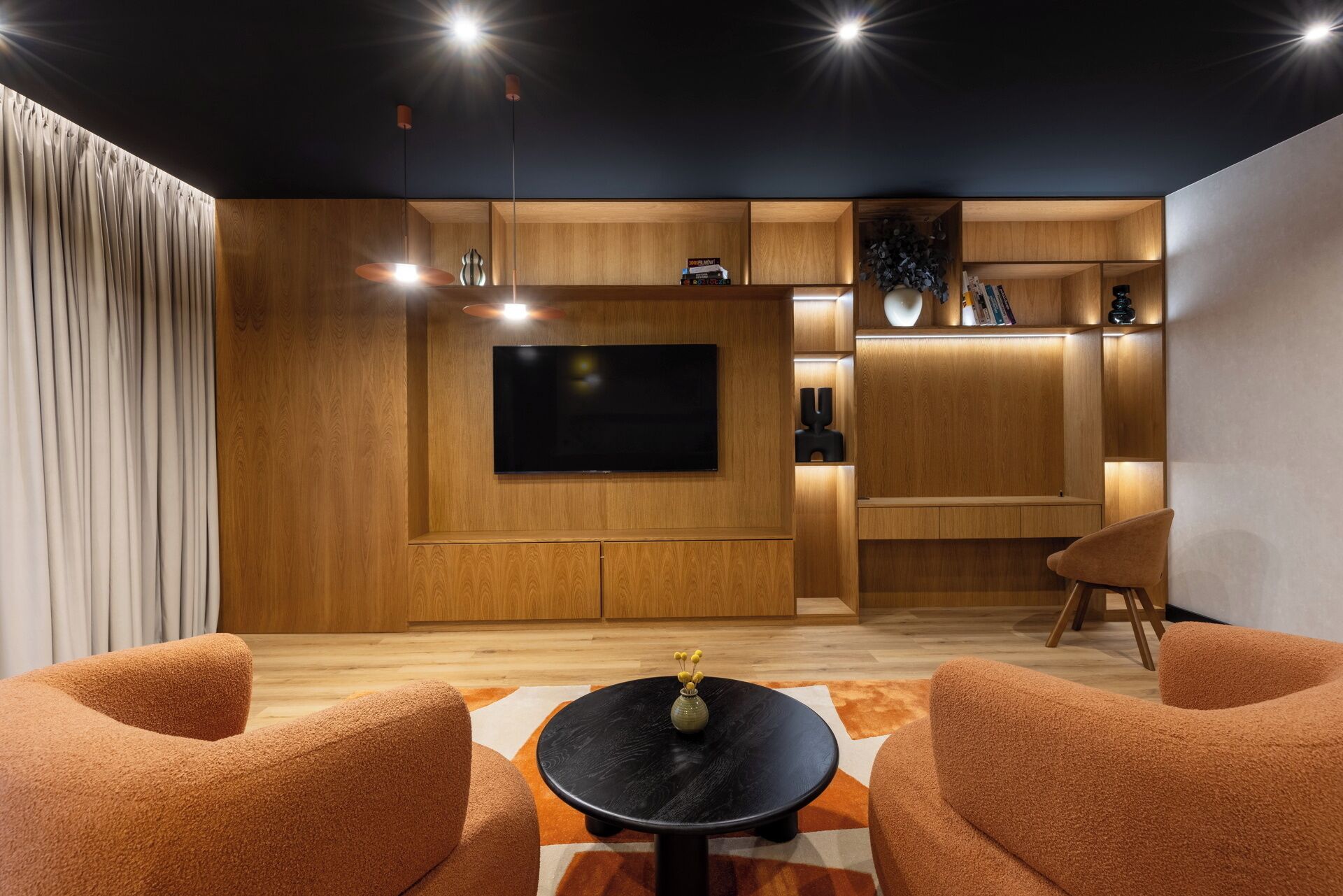A modern living room with a flat-screen TV, wooden cabinetry, and a cozy seating area with two armchairs and a coffee table.