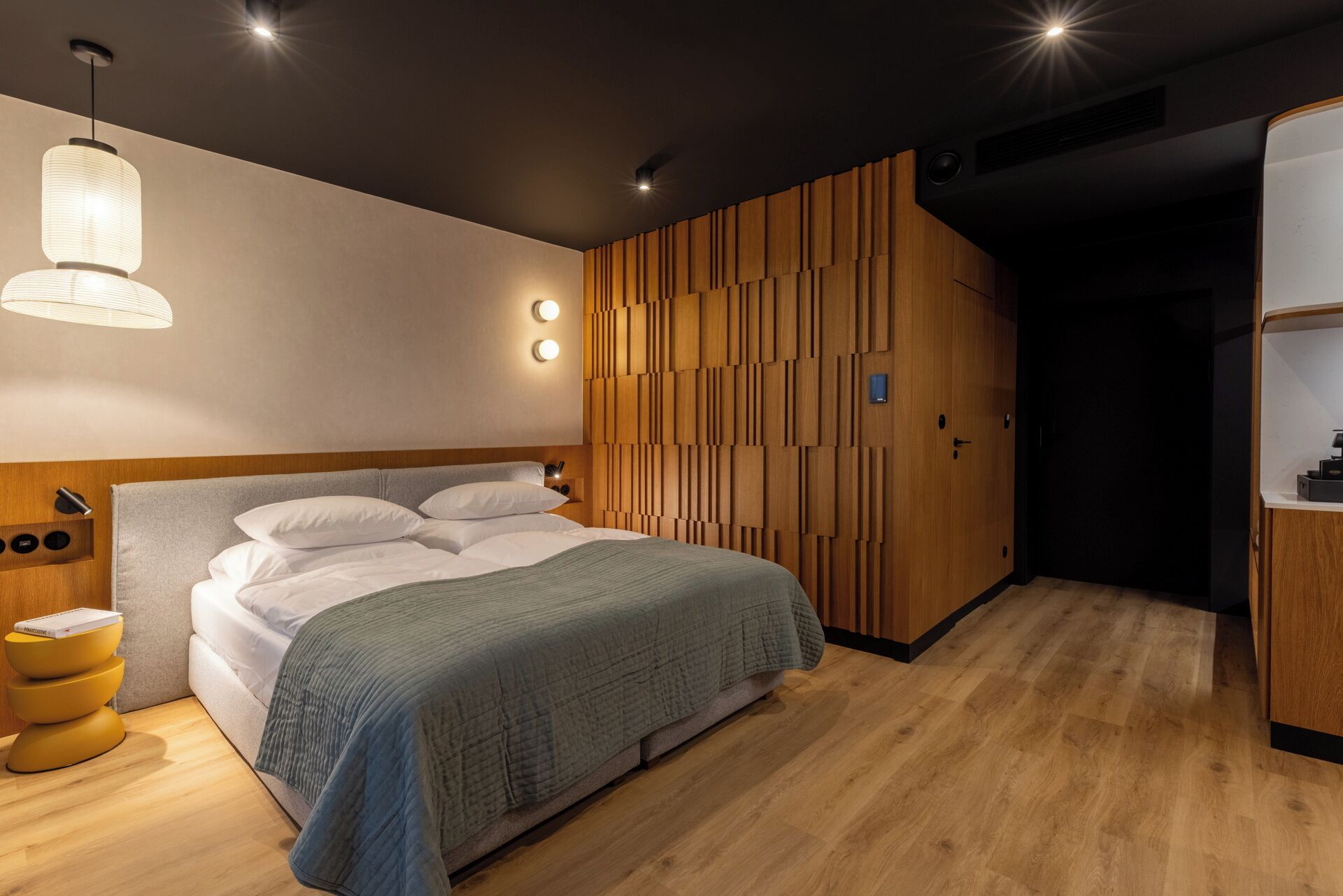 Een moderne slaapkamer met een houten hoofdbord, een bed met wit beddengoed, een nachtkastje met een lamp en een houten garderobe.