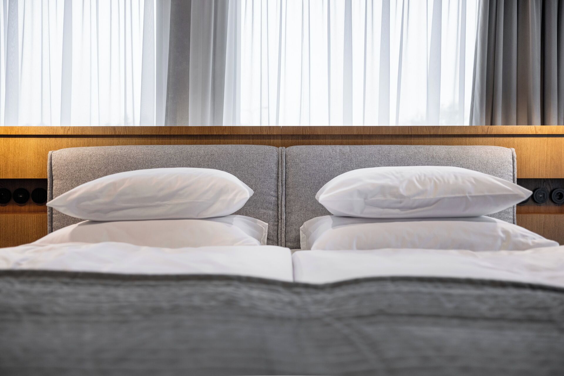Une chambre d’hôtel avec un lit double, une tête de lit grise et du linge de lit blanc.
