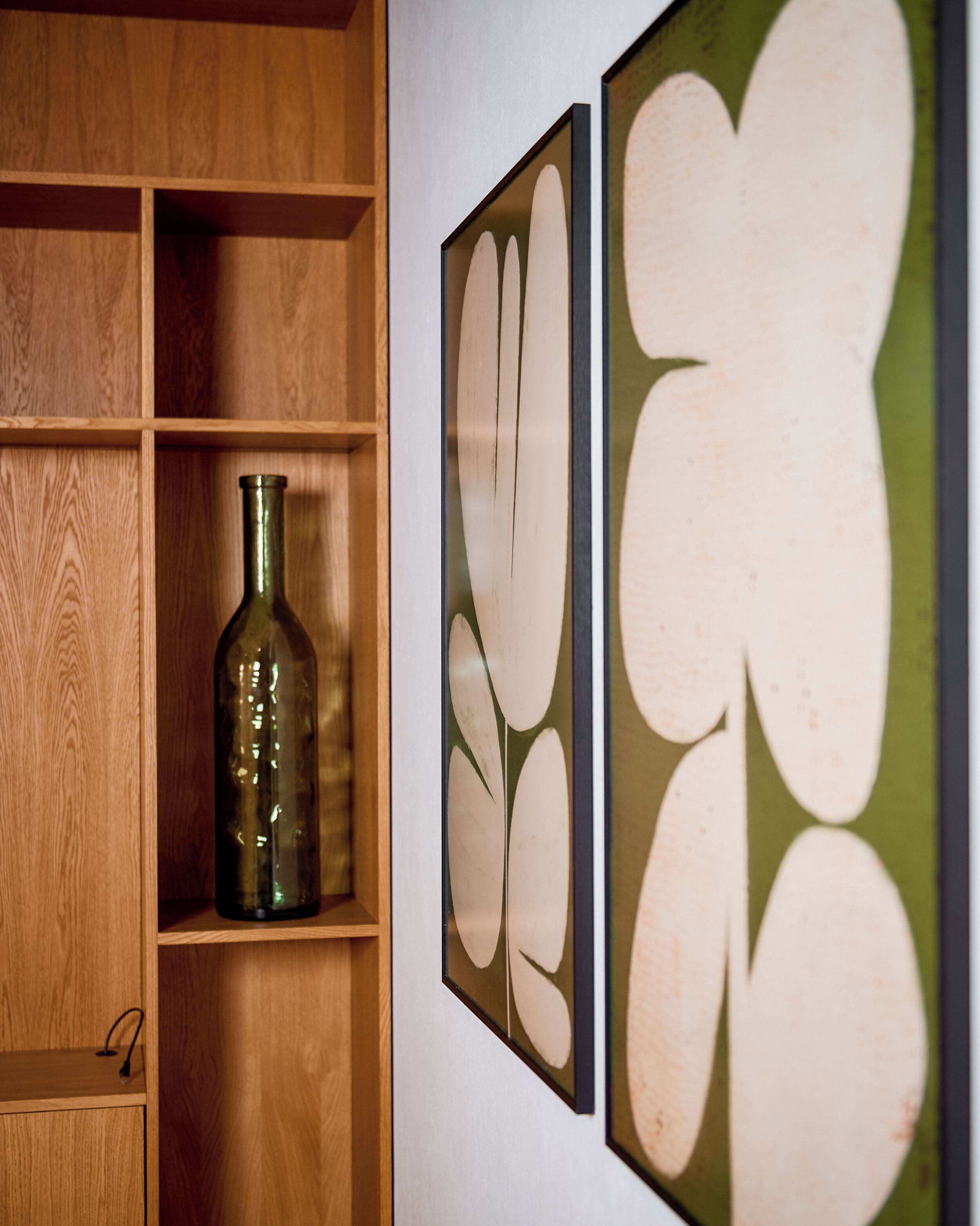 Une étagère en bois sur laquelle sont posés un flacon en verre vert et deux œuvres d’art encadrées destinées à être accrochées au mur.