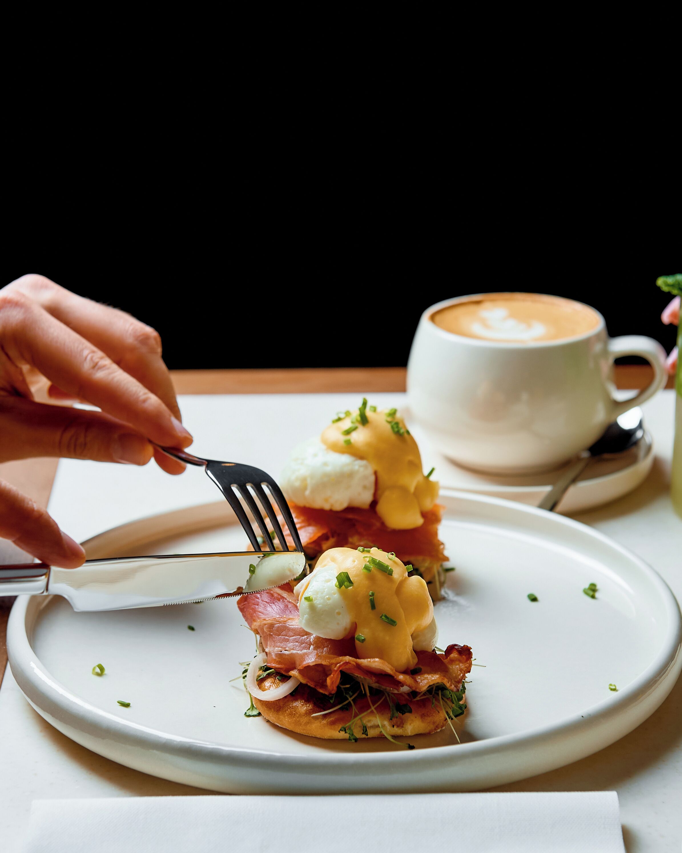 A breakfast plate with eggs benedict, bacon, and a cup of coffee.