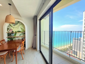 A balcony with a view of the sea and buildings, a dining area with a table and chairs, and a hanging light fixture. - Apartment With Balcony (Nha Trang)