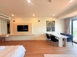 A hotel room with a bed, a TV mounted on the wall, a dining table with chairs, and a large window. - Apartment With Balcony (Nha Trang)