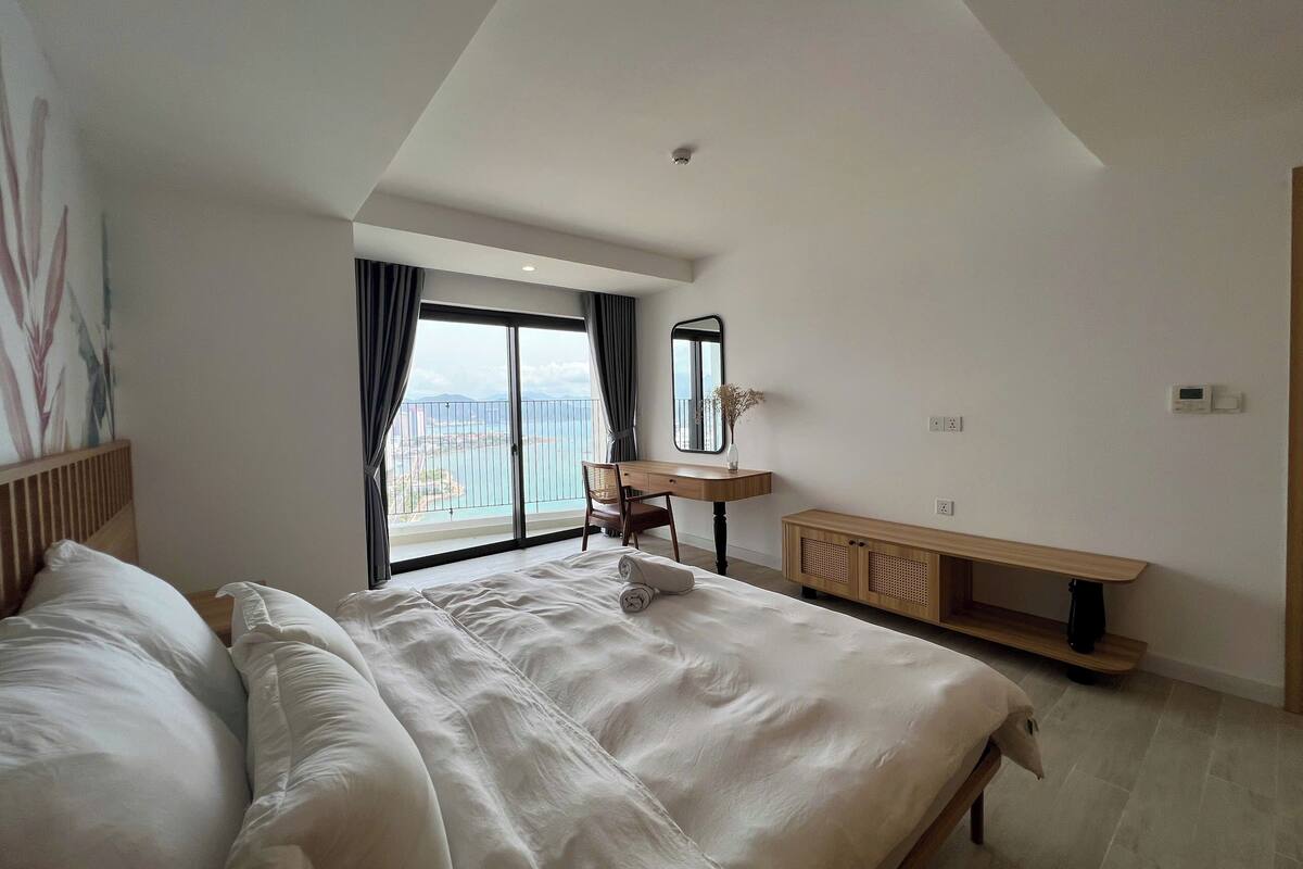 Ein modernes Hotelzimmer mit einem großen Bett, einem Schreibtisch und Meerblick vom Balkon aus.