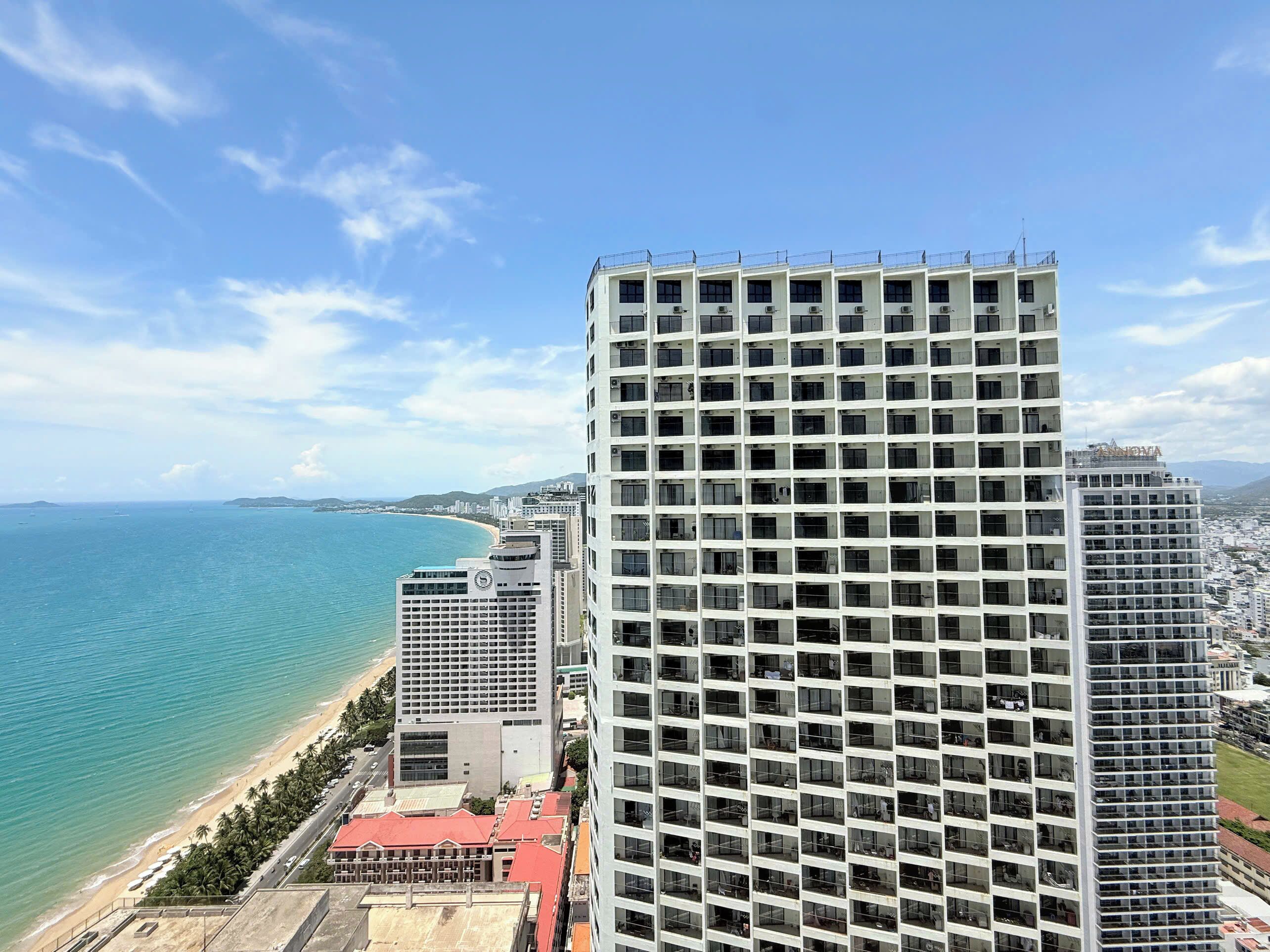 A high-rise building with a grid of windows, adjacent to a beach and ocean.