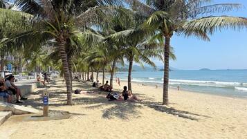 A beach with palm trees, people relaxing, and a clear sky.