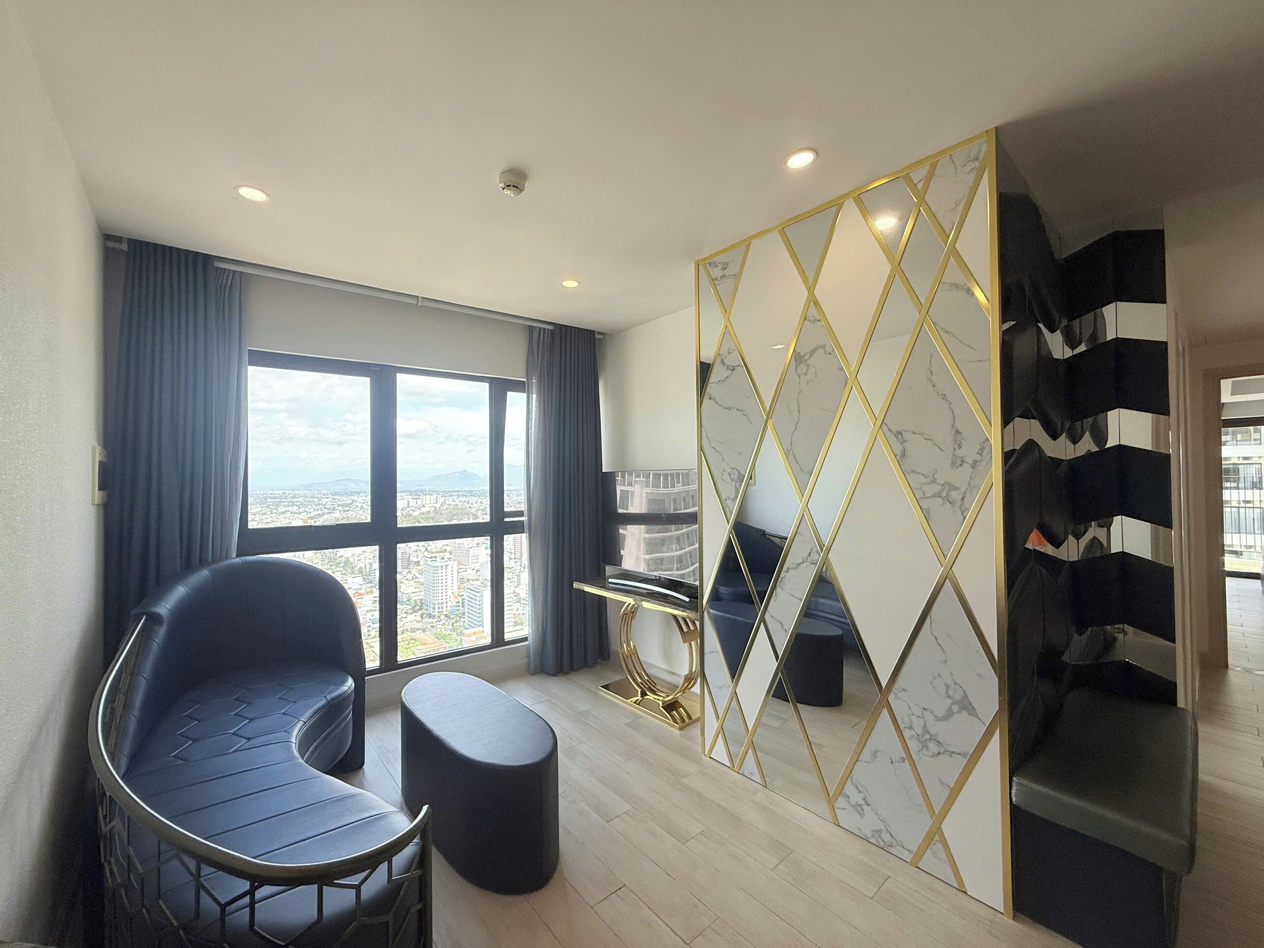 A modern room with a curved black chair, a small ottoman, a marble-patterned partition, and a view of a cityscape through a large window.