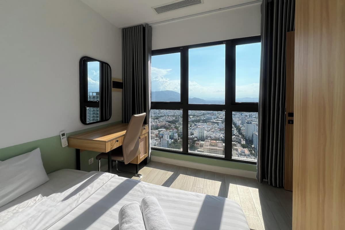 Ein Hotelzimmer mit großem Fenster und Blick auf die Stadt, einem Bett, einem Schreibtisch und einem Stuhl.
