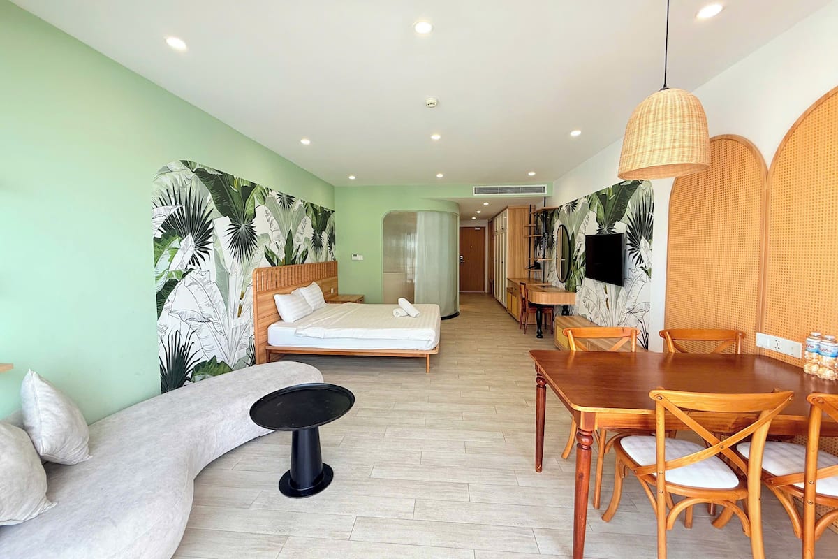 Ein Hotelzimmer mit Bett, einem Esstisch mit Stühlen, einem kleinen runden Tisch und einem an der Wand befestigten Fernseher.