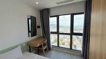 A hotel room with a bed, a desk, a chair, and a large window offering a city view.