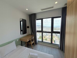 Une chambre d’hôtel équipée d’un lit, d’un bureau, d’une chaise et d’une grande fenêtre donnant sur la ville.