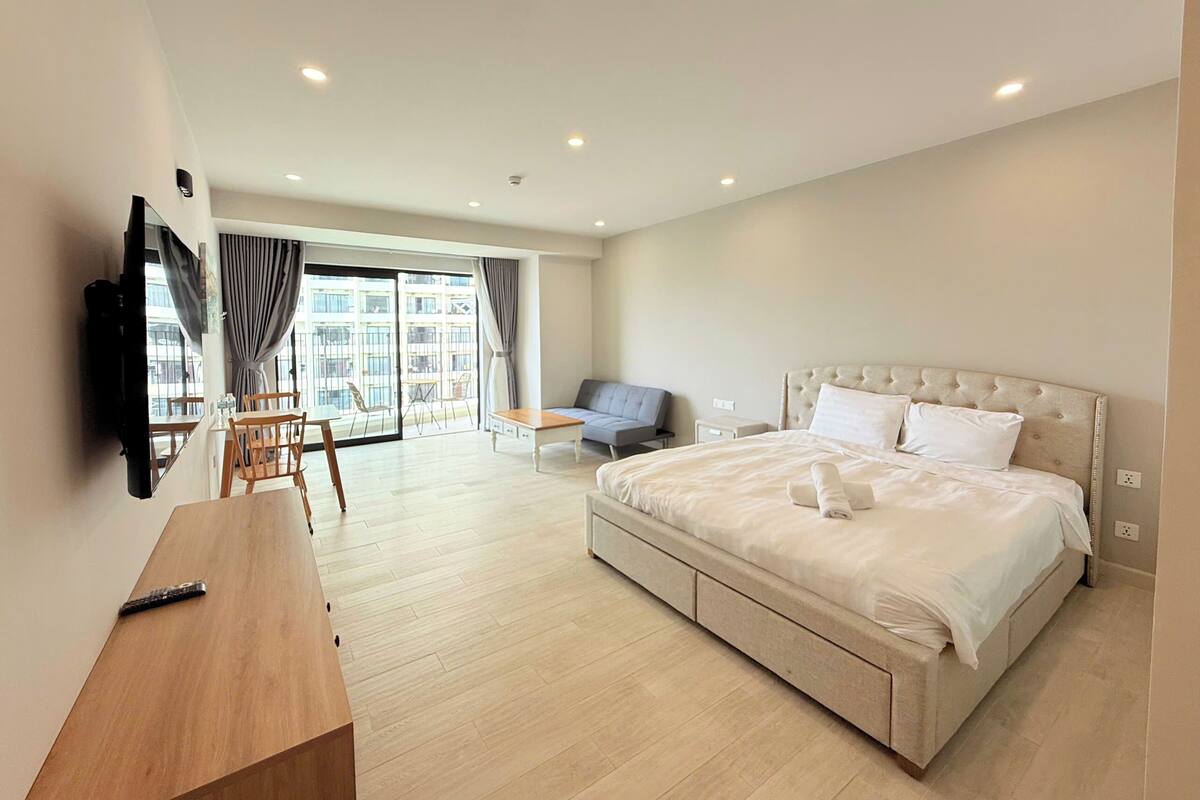 Ein modernes Hotelzimmer mit einem großen Bett, einem Schreibtisch, einem Sessel und einem an der Wand befestigten Fernseher.